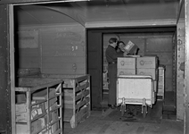 803497 Afbeelding van het beladen van een goederenwagen met pakketten (stukgoederen) in de loods van Van Gend & Loos te ...